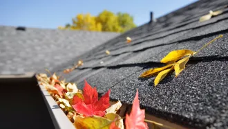 Steildach welches mit dem Blättern vom Herbst in der Regenrinne bedeckt ist 